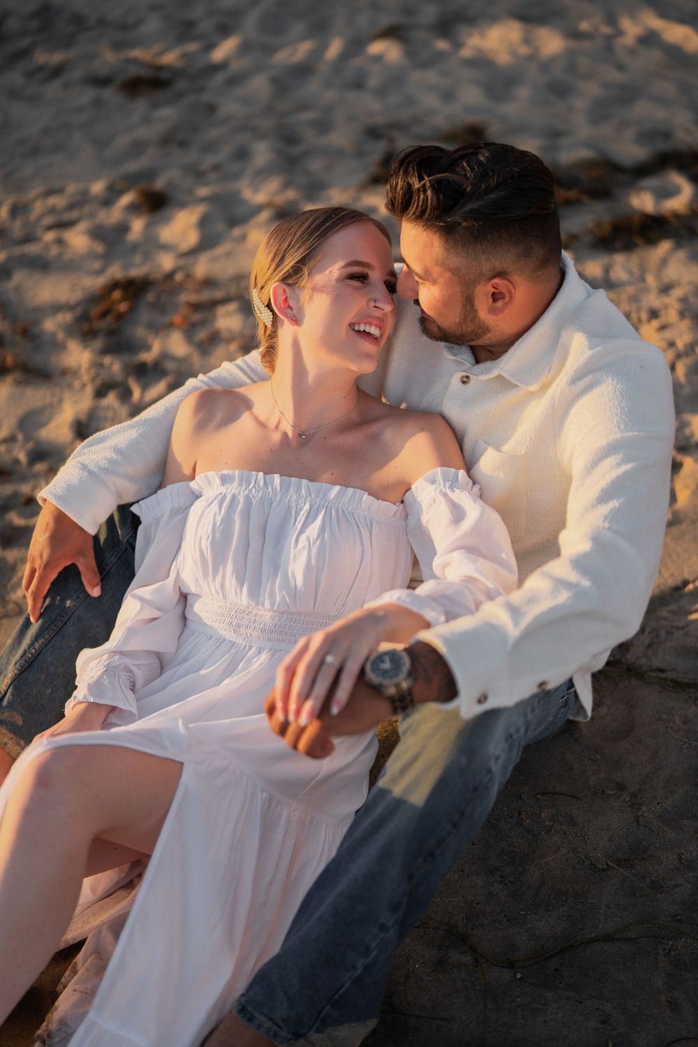 A couple shares a laugh while sitting on coastal rocks at sunset.