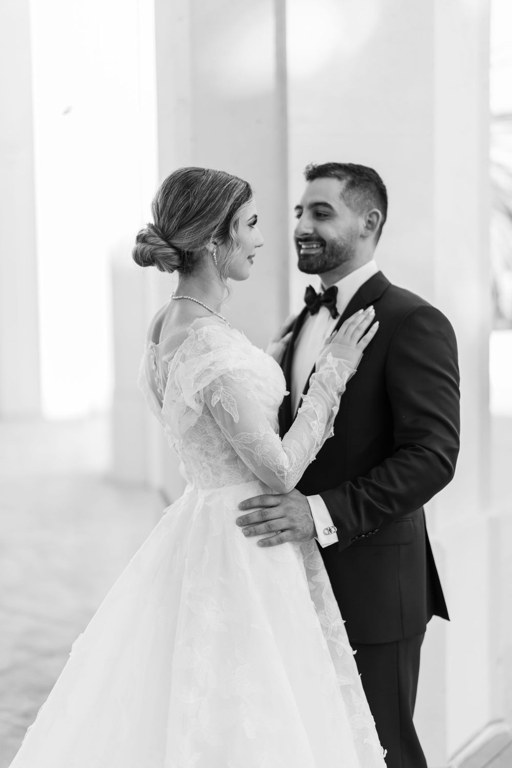 Black and white portrait of newlyweds sharing an intimate moment in a columned venue.