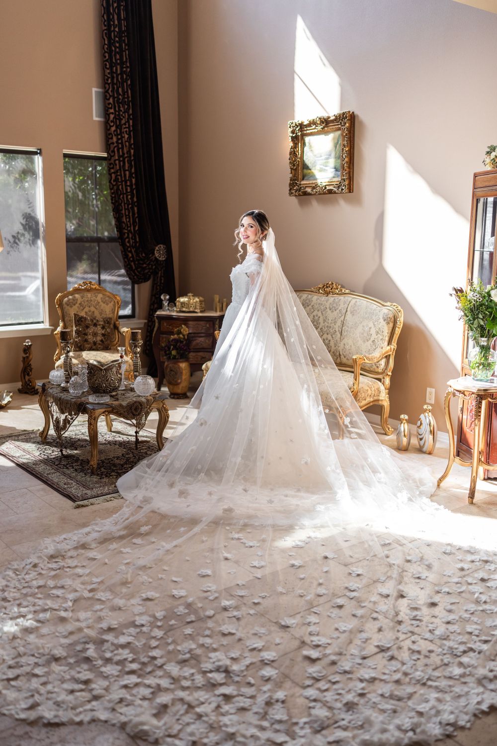 Elegant wedding dress with cathedral length lace veil in sunlit room with antique furniture.