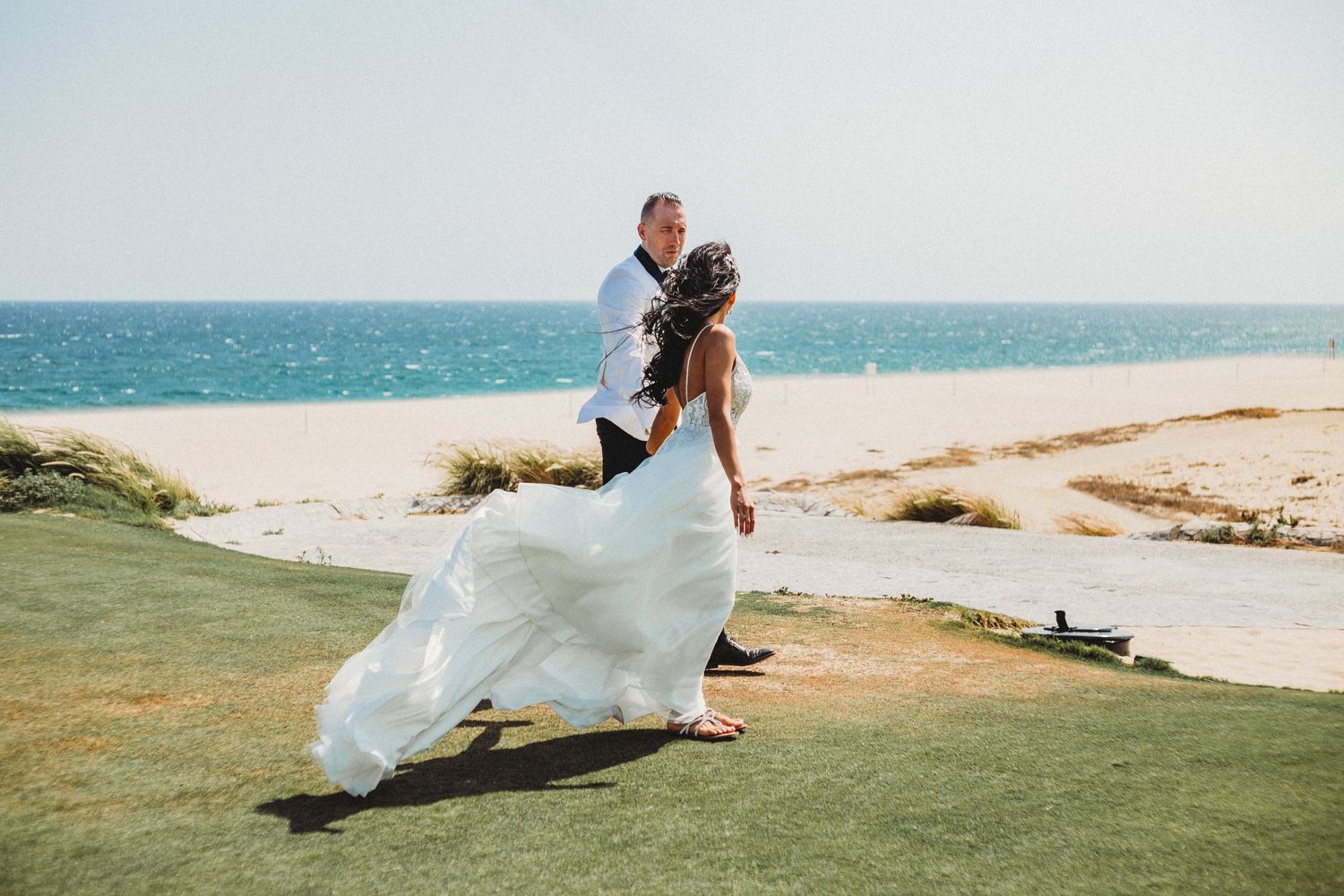 Man and wife walking in the wind on a mexico golf course in Cabo after their wedding.