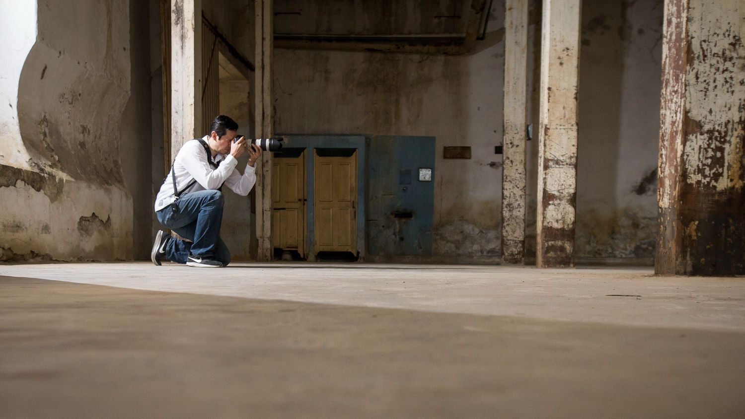 A photographer crouches to capture a shot in an industrial concrete space.
