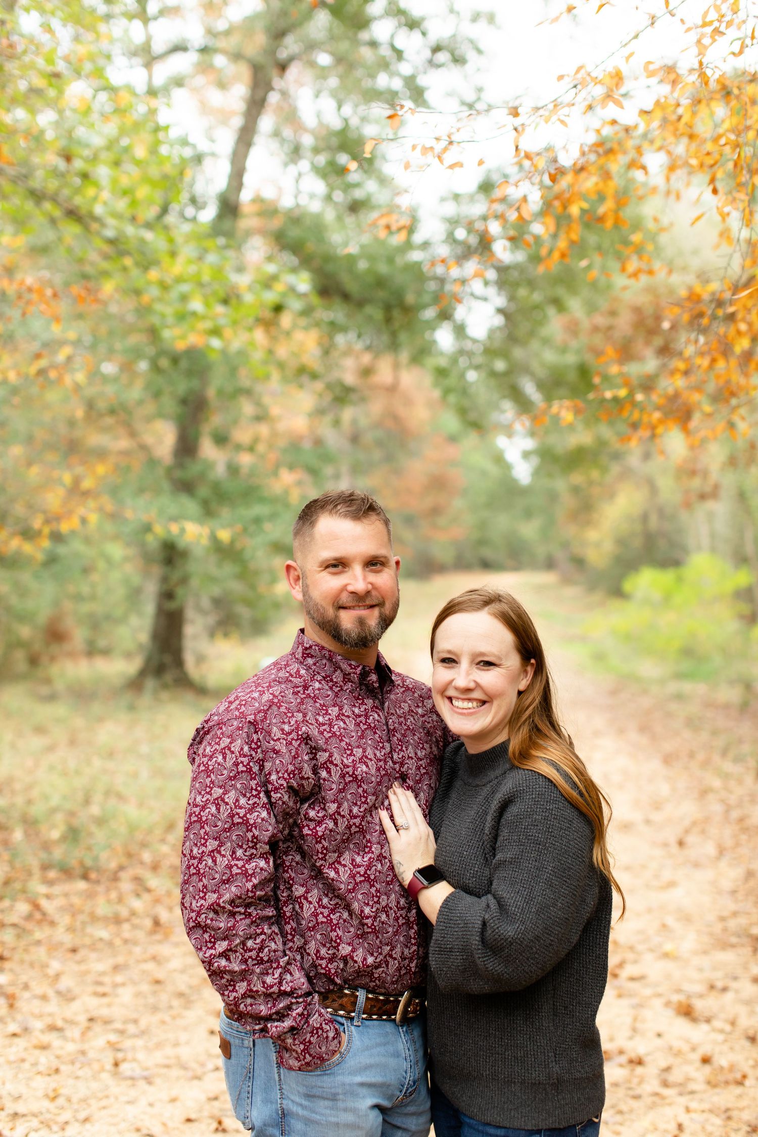 Couple posing together on forest path surrounded by fall foliage.