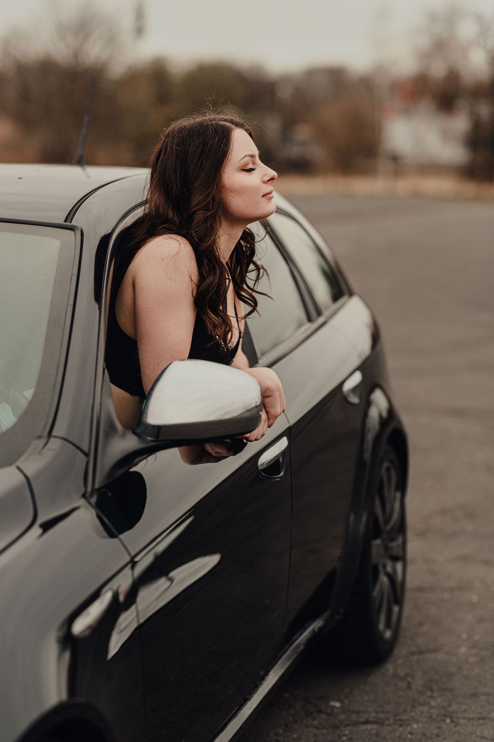Moody car photoshoot with model leaning out of silver vehicle window.