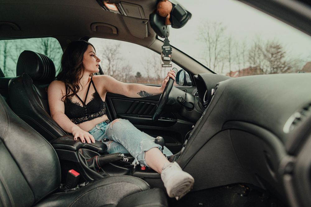 A car interior shot showing someone sitting in the driver's seat wearing black clothing.