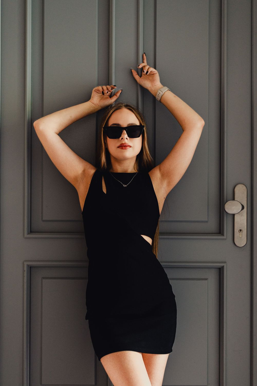 Dramatic poses against grey door wearing black outfit and sunglasses.