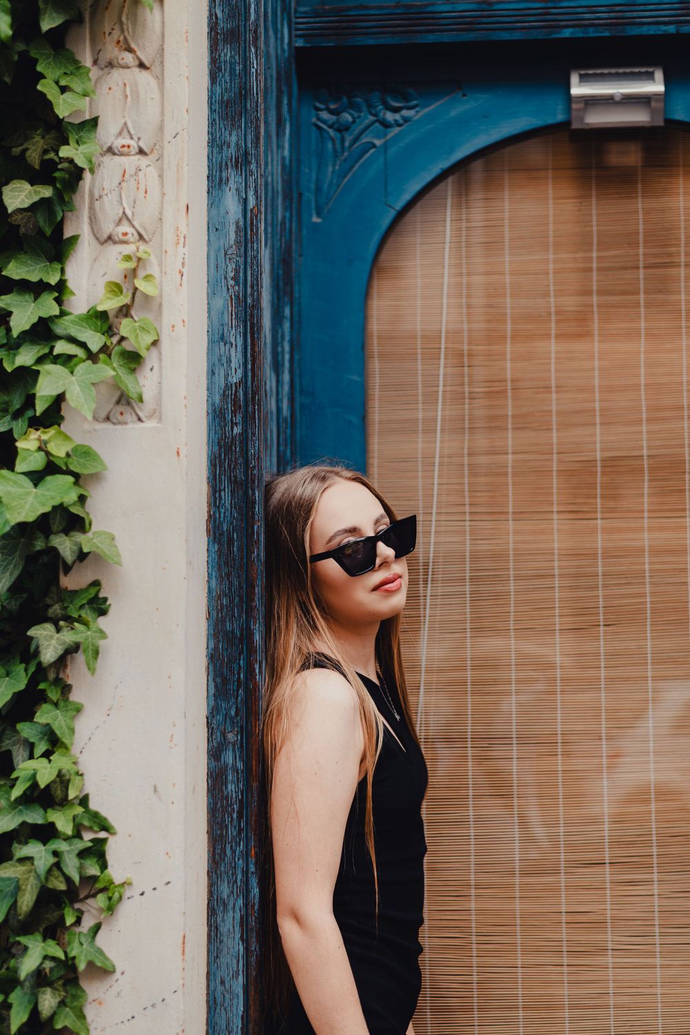 Stylish portrait near blue door frame with ivy and bamboo blinds.