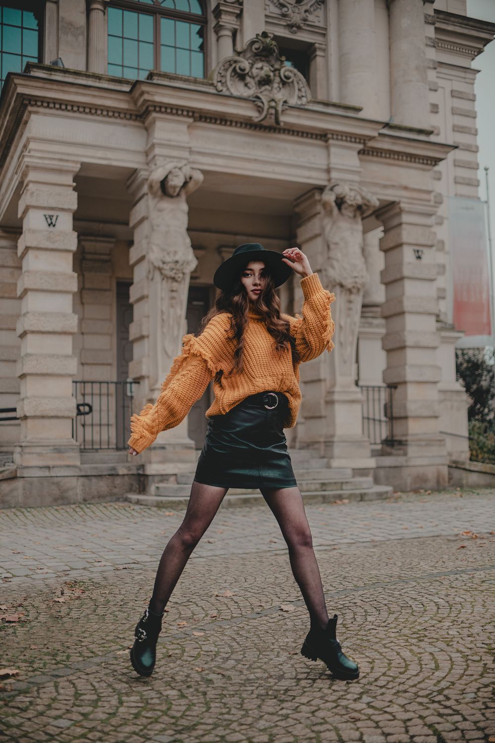 Playful fashion shoot in front of historic architecture wearing mustard sweater and black boots.