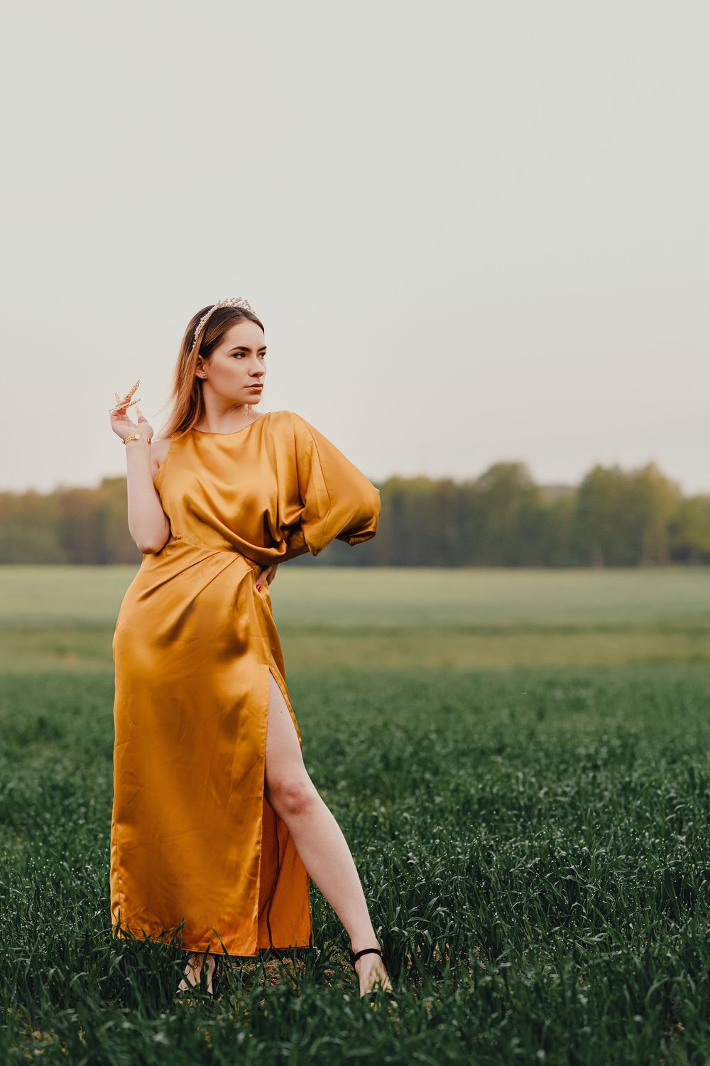 Fashion portrait in a golden silk dress posing dramatically in a grassy field at sunset.