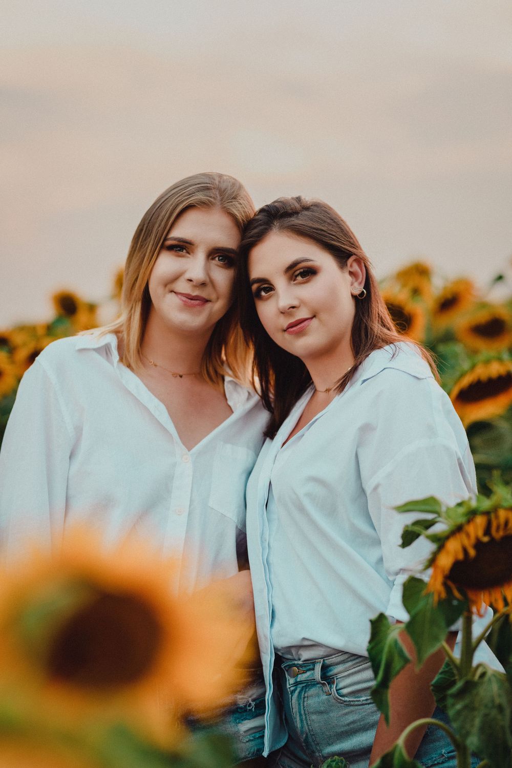 Two people in matching light blue shirts pose together among blooming sunflowers.