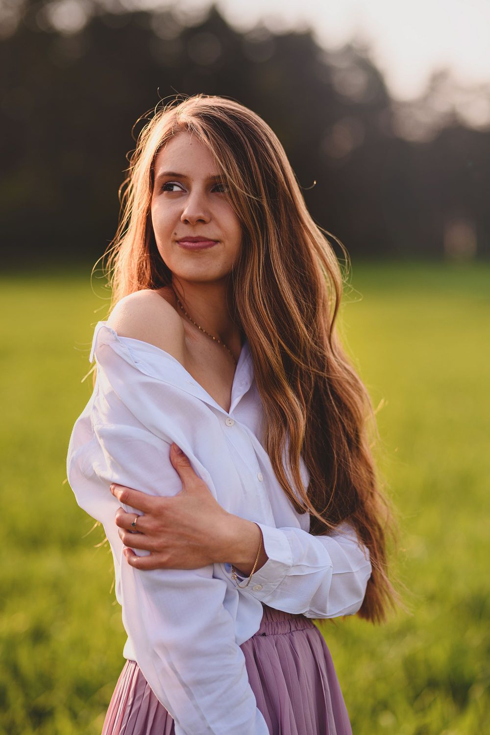 Portrait of a woman in white shirt and pink skirt standing in a sunlit meadow at golden hour.