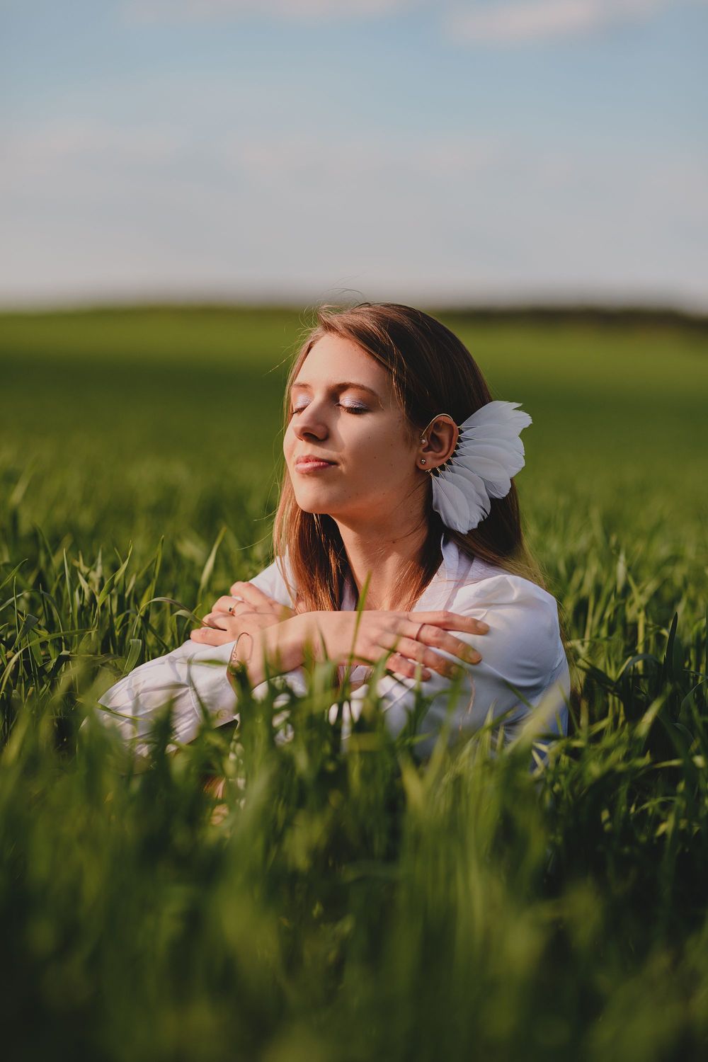 Dreamy outdoor portrait in a green wheat field with a white butterfly hair accessory.