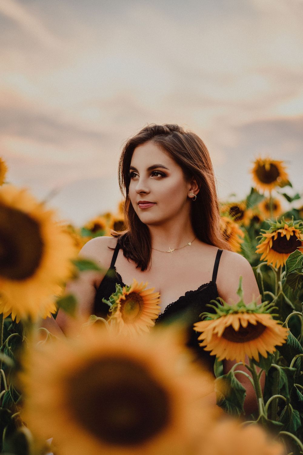 Person in black top poses among tall sunflowers during golden hour.