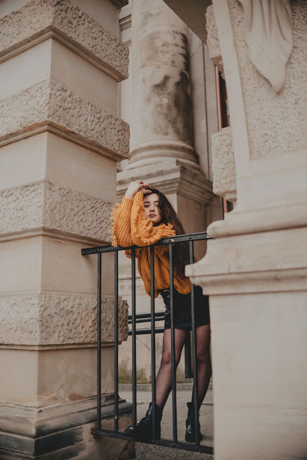 Fashion editorial shot against stone building featuring mustard sweater and architectural elements.