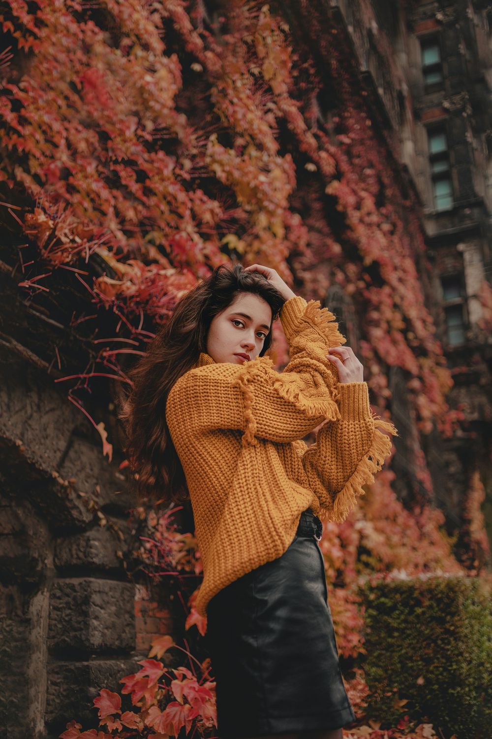 Autumn fashion photography with orange knit sweater against vibrant red fall foliage.