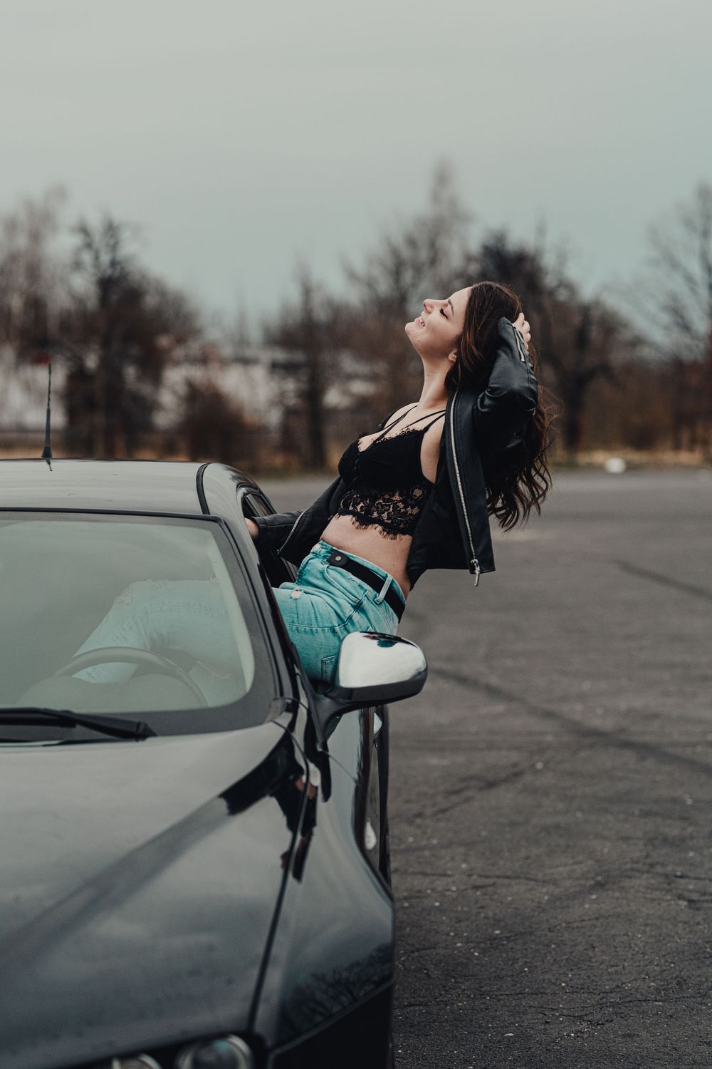 Person leaning out of a car window in an artistic pose against a cloudy sky.