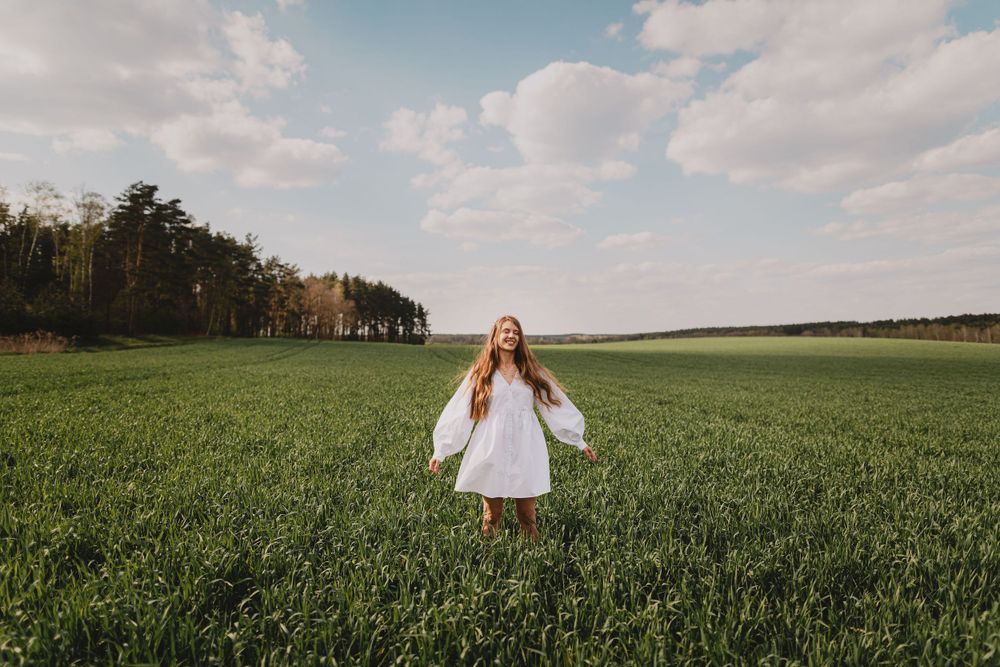 Panoramic view of person in vast green field under cloudy sky.