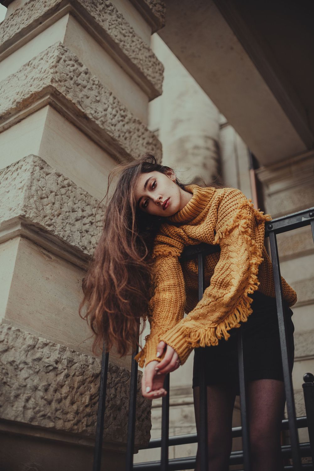 Stylish autumn outfit with oversized sweater posed against classical architecture and railing.