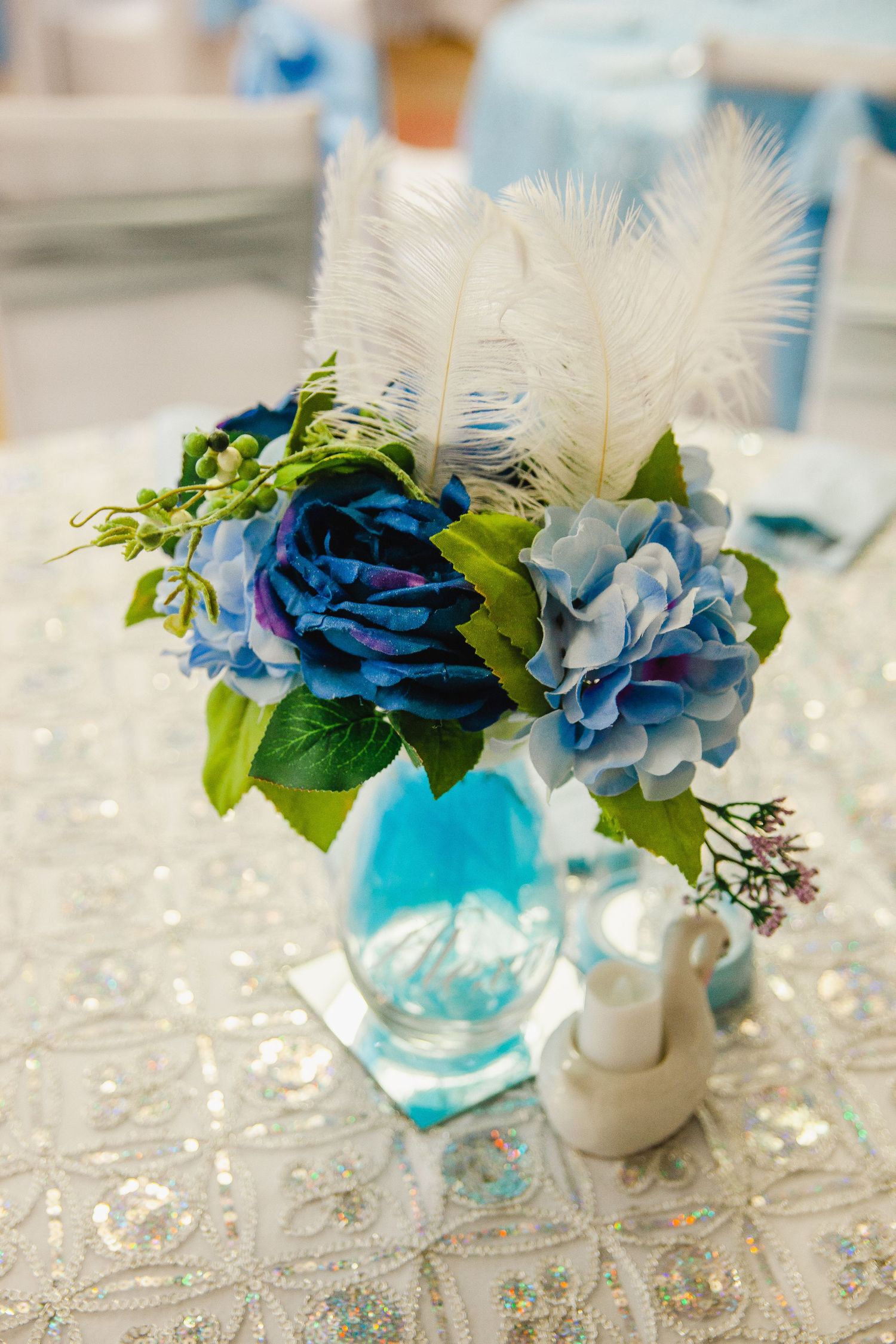 Turquoise vases with blue flowers and white feathers as elegant centerpieces.