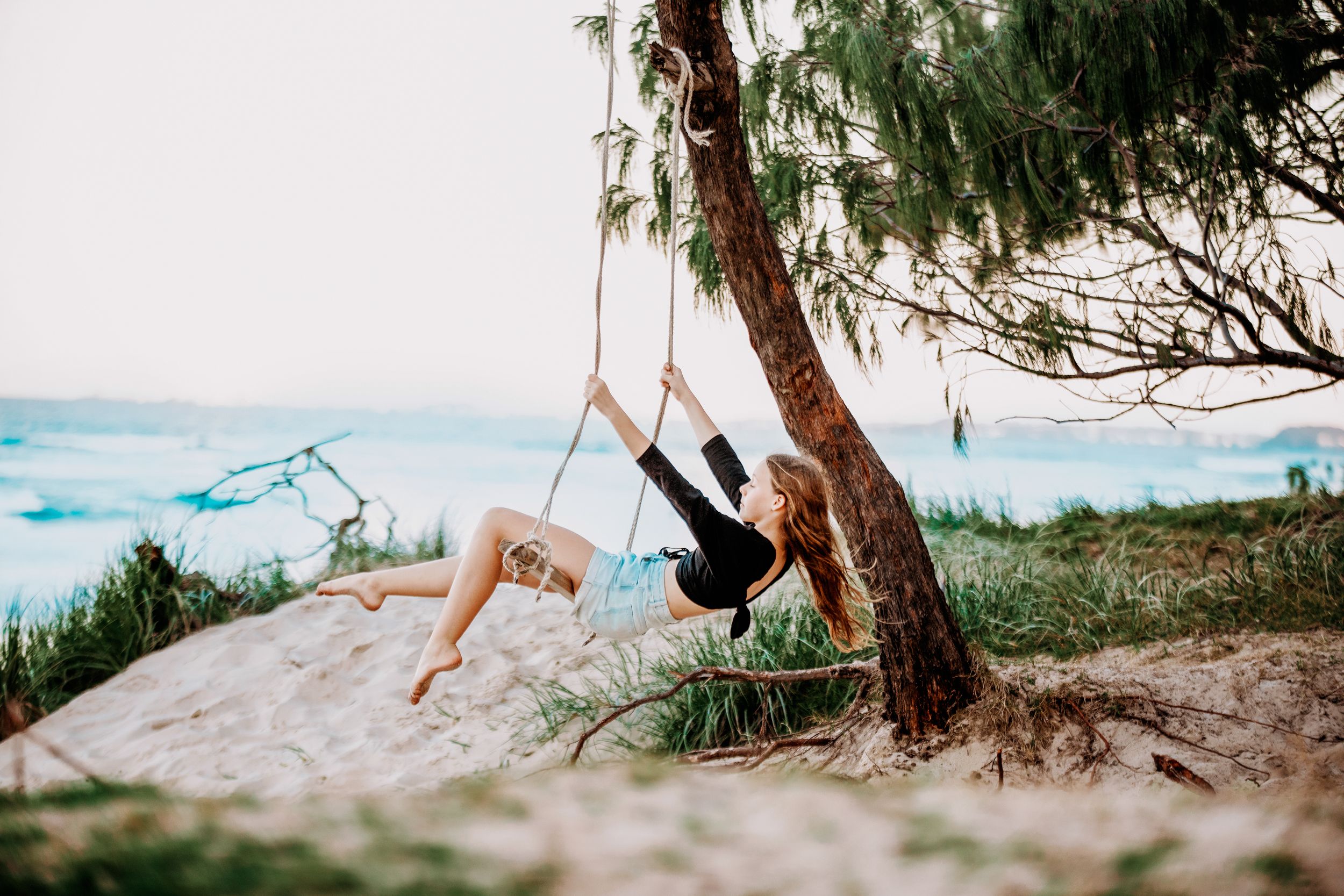 A silhouette of someone swinging on a rope swing by the beach at sunset.