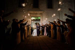 Wedding guests hold sparklers creating a magical tunnel effect at night during the couple's exit.