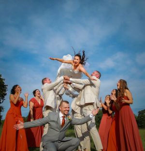 Wedding party in red dresses and gray suits poses for fun jumping photos outdoors.