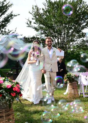 Newlyweds walk through magical bubble-filled garden after outdoor ceremony.