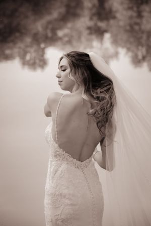 Elegant bride in lace wedding dress with buttons shows details of gown in sepia tones.