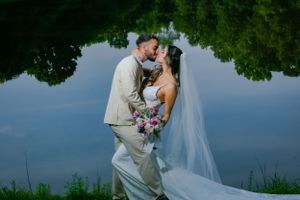 Wedding couple embraces by waterfront under dramatic stormy sky.