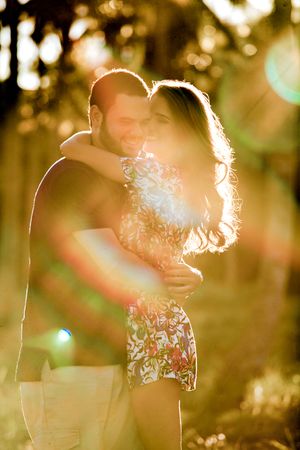Romantic wedding couple embraces in soft golden sunlight with bokeh effects in background.