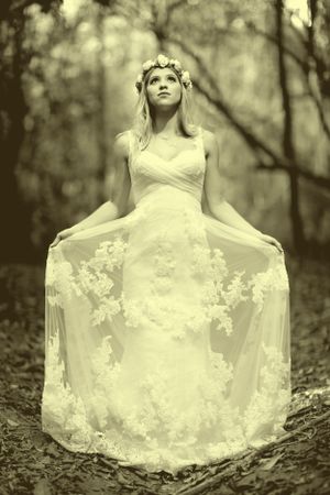 Ethereal bridal portrait in lace dress against dreamy forest backdrop.