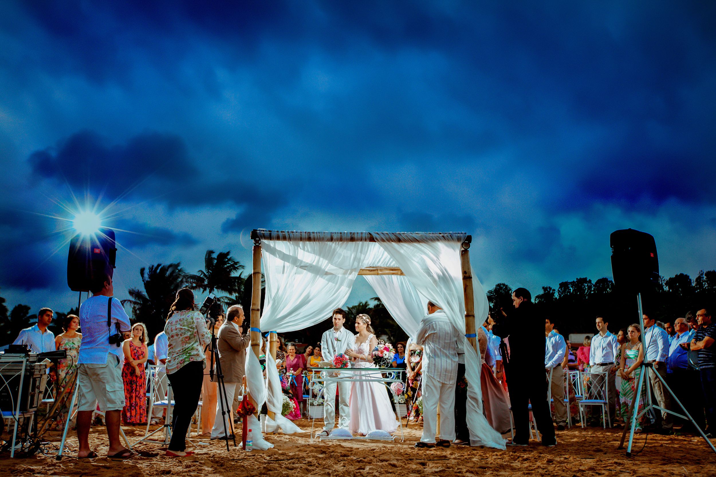 Dramatic blue sky wedding ceremony setup with white tent and guests silhouetted against the horizon.