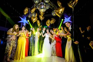 Large group wearing colorful formal attire poses together under dramatic lighting.