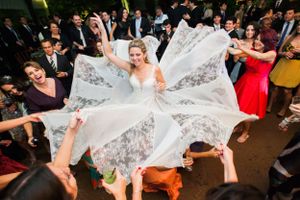 A bride's dress spreads in a circle as wedding guests lift and spin her during a reception dance.