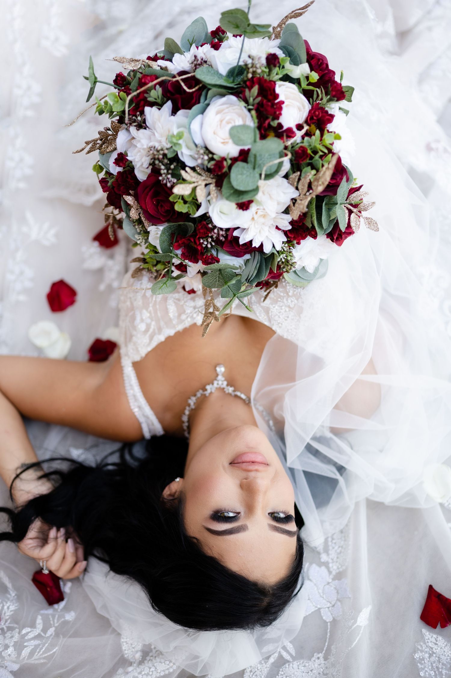 A stunning bridal bouquet with burgundy and white flowers paired with eucalyptus leaves on white fabric.