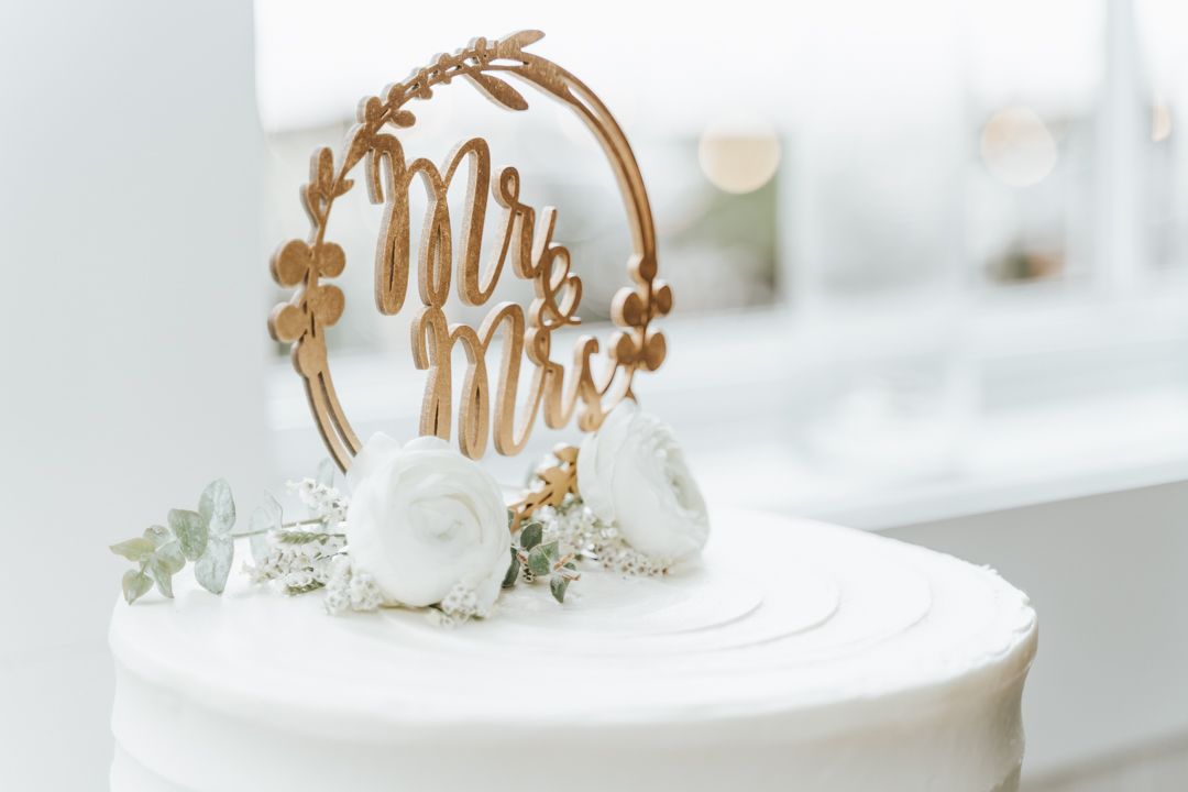 Elegant 'Mr & Mrs' gold cake topper with white flowers on white wedding cake.