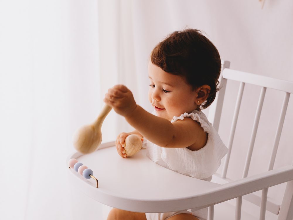Young child in a white chair reaching for something while playing.