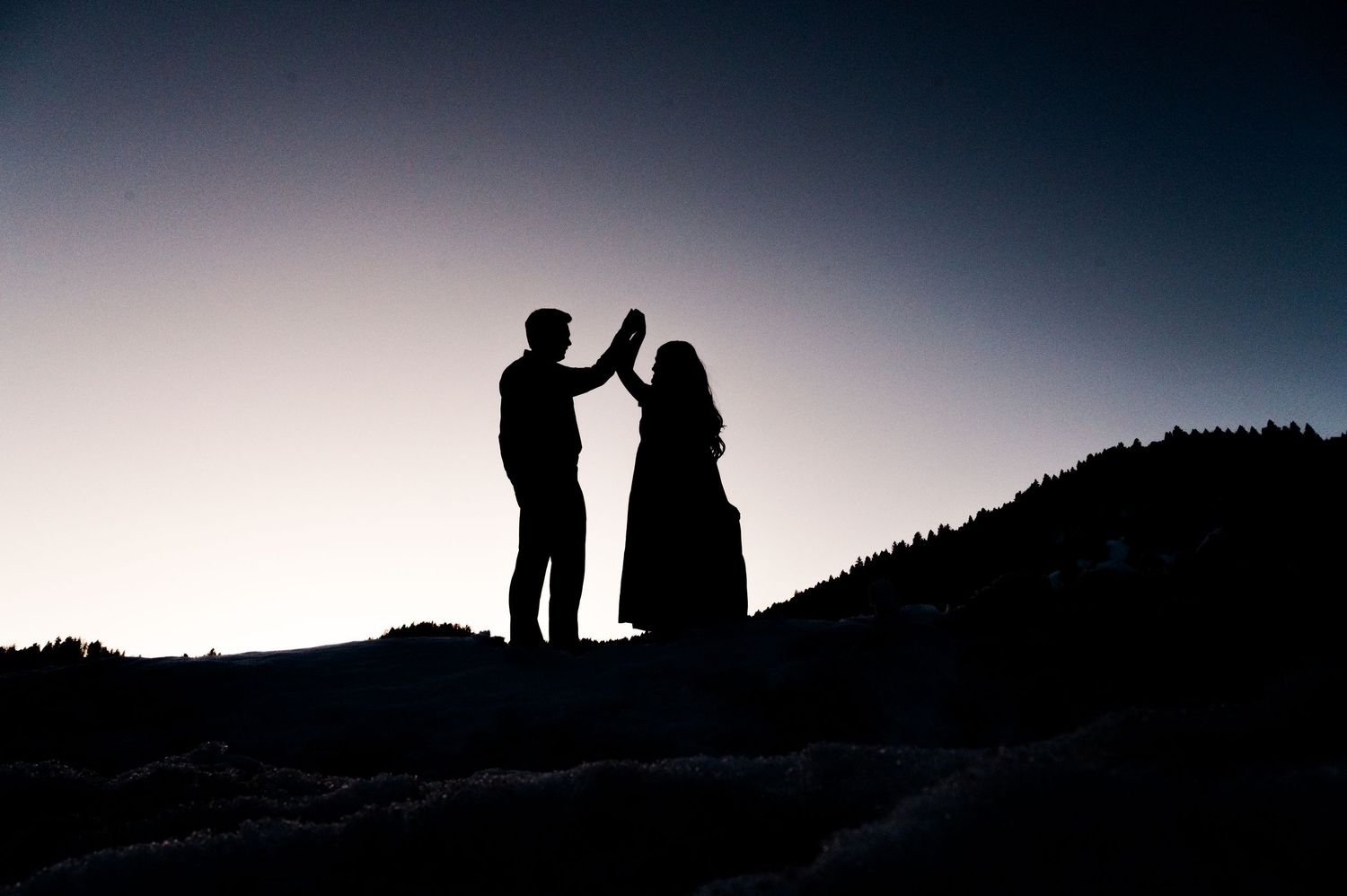 Silhouettes of two people dancing on a hilltop against a sunset sky.
