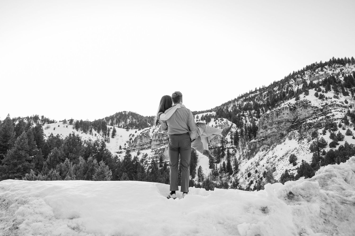 A black and white photo of a couple standing in a snowy mountain landscape.