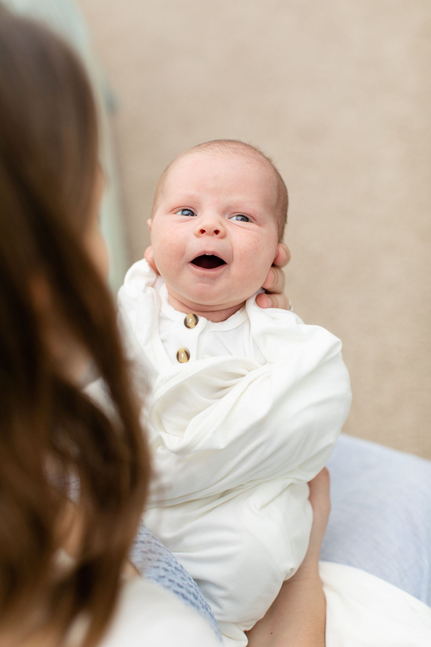 Happy baby in white outfit smiling with wide open expression.