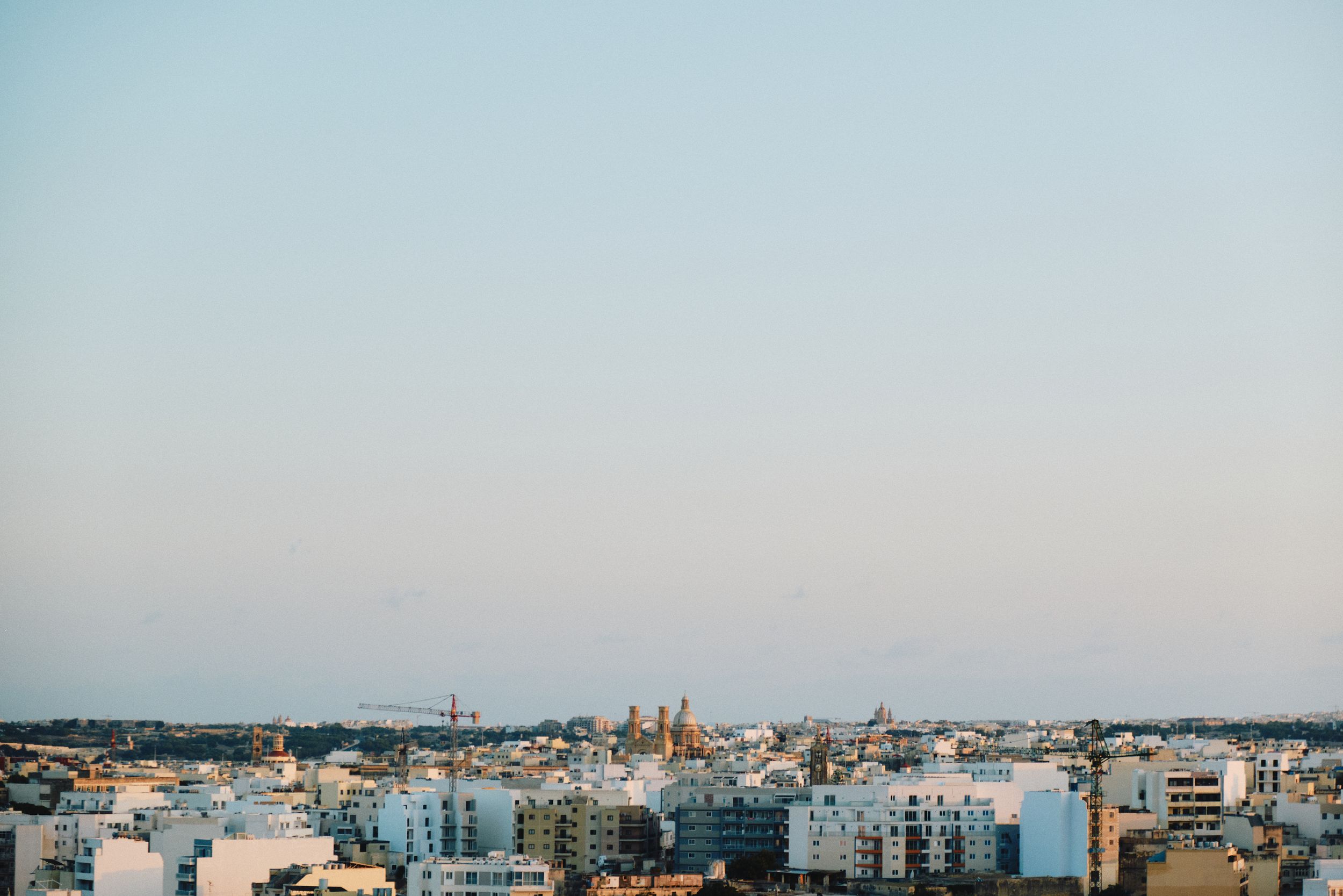 Panoramic cityscape view of Malta with church domes and buildings during dusk.