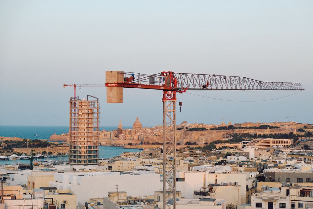 Large construction crane overlooking Malta's coastal cityscape and harbor.