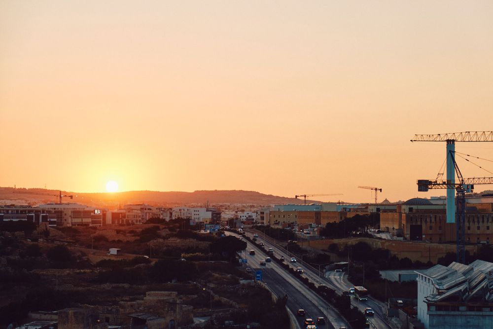 Construction cranes tower over a Mediterranean city during golden sunset.