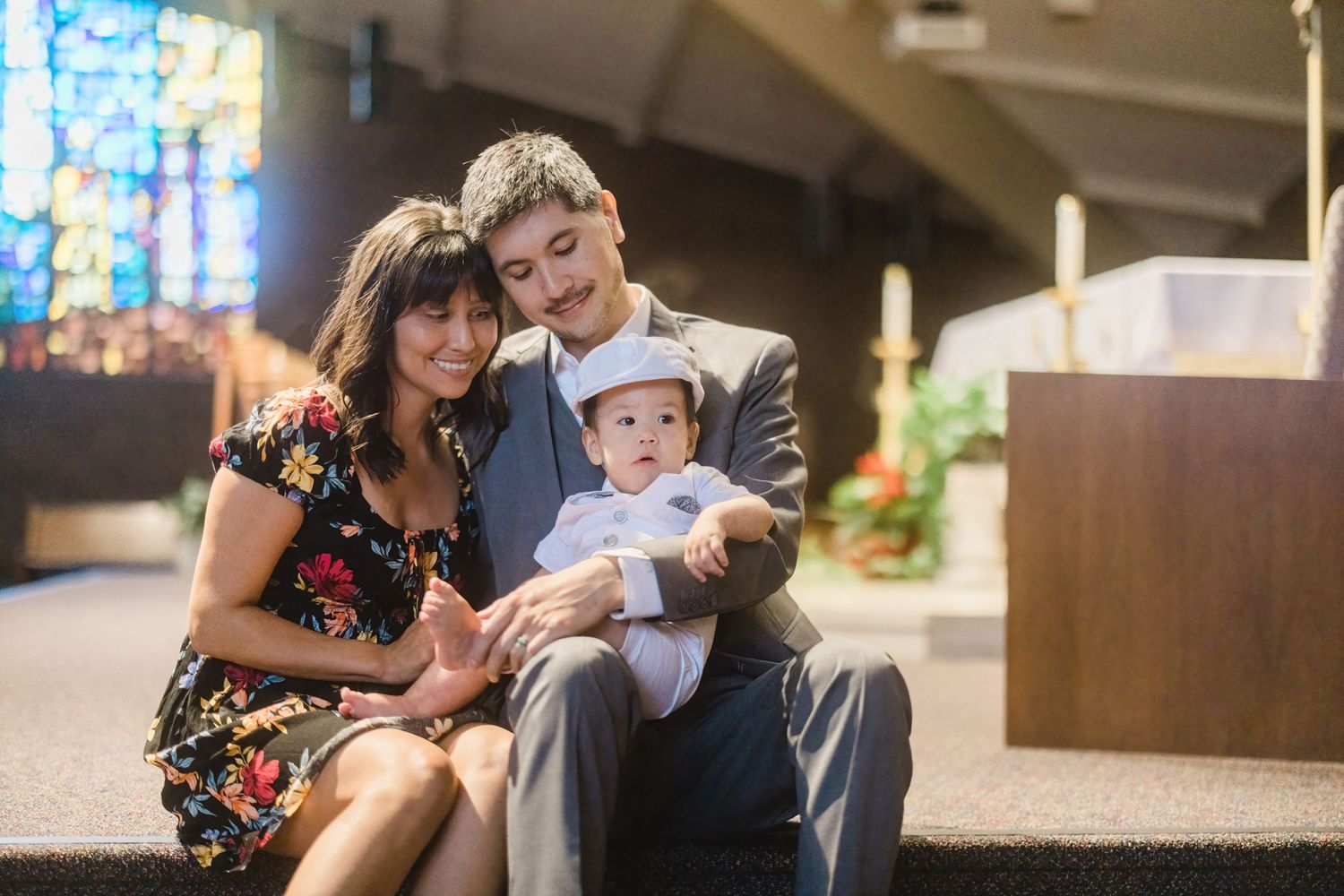 A family sits together in a church pew with stained glass windows in the background.