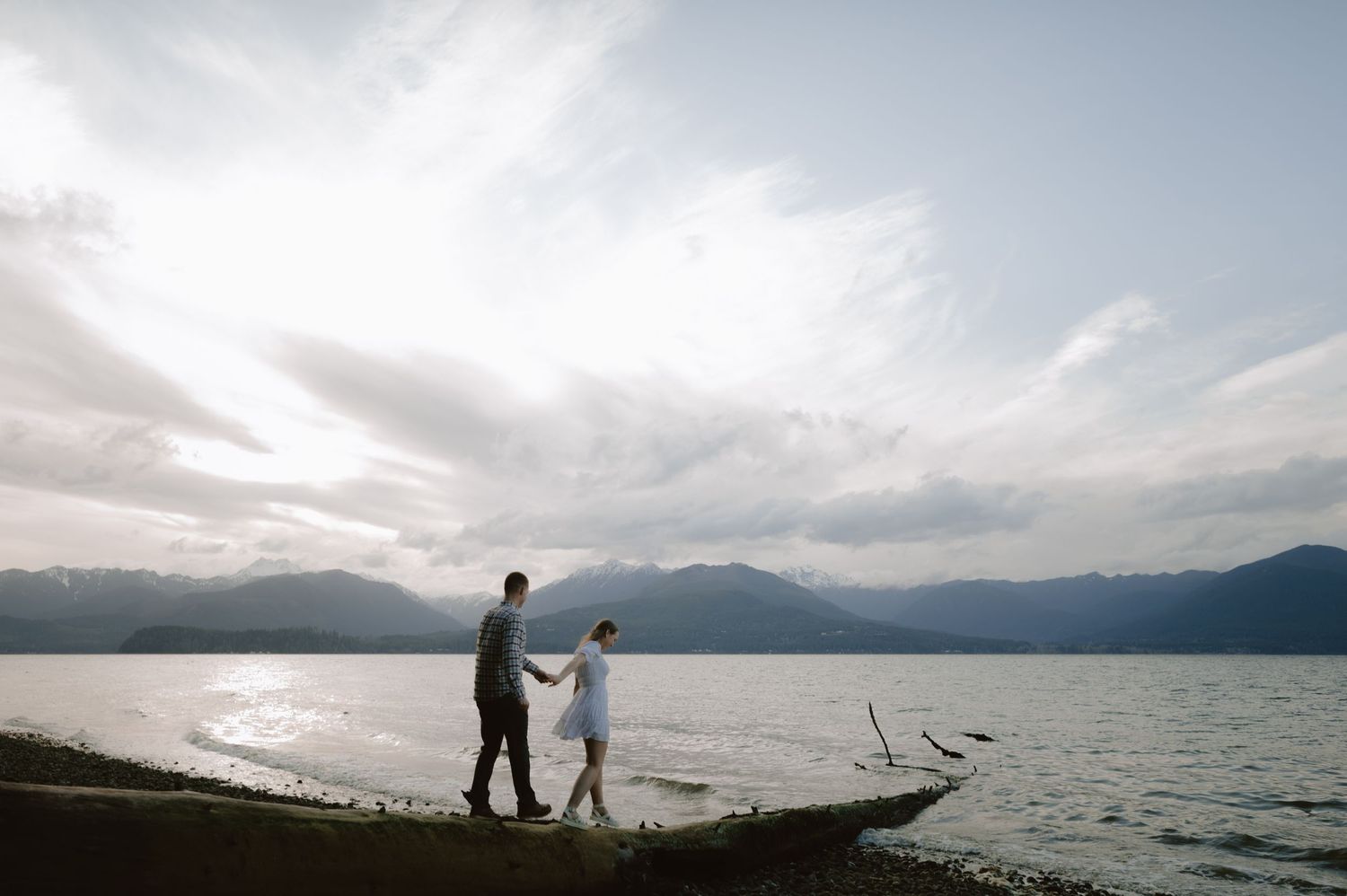 Silhouetted couple walking along a lakeside with mountains in the background.
