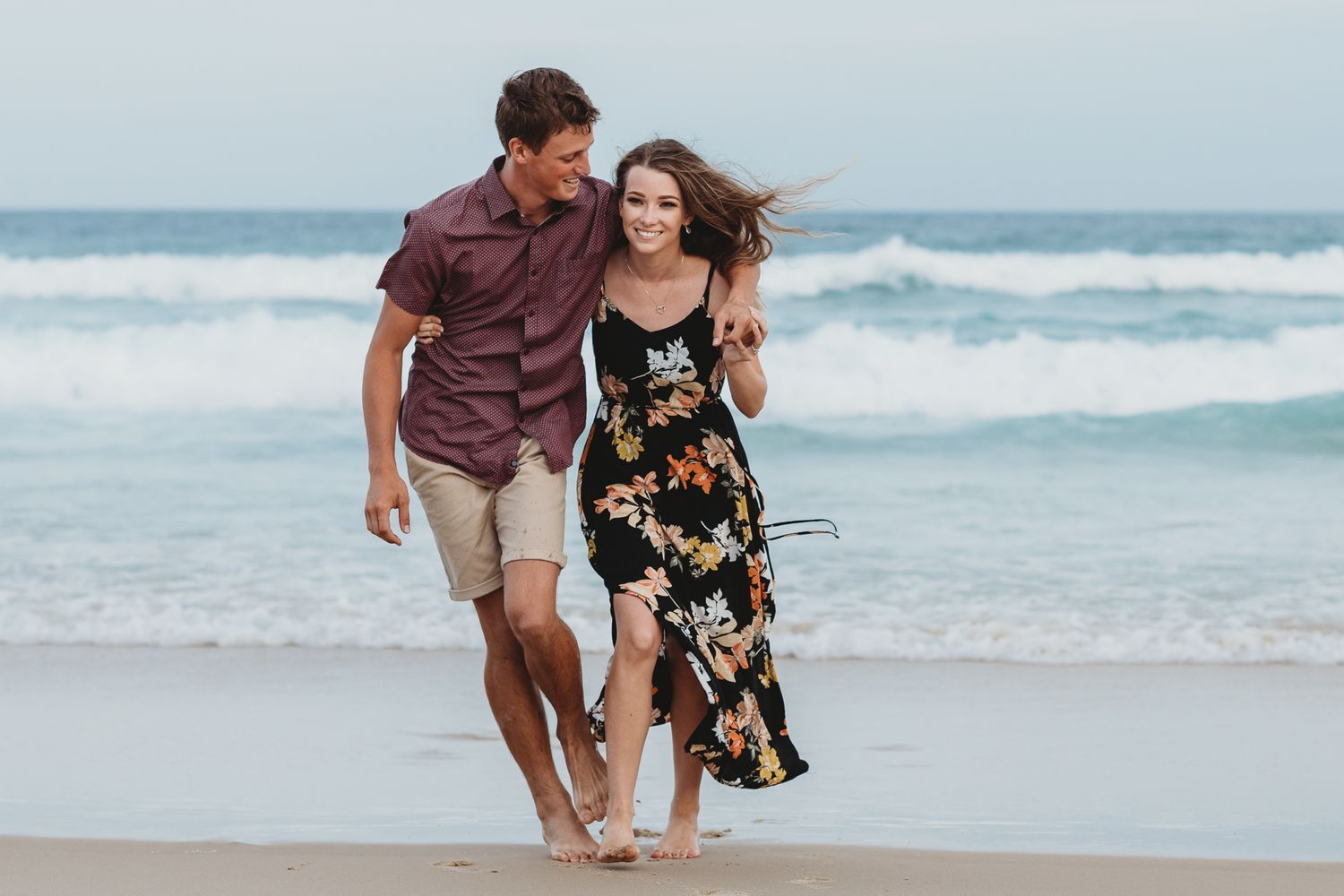 Couple walking together along beach shoreline with waves crashing behind them.