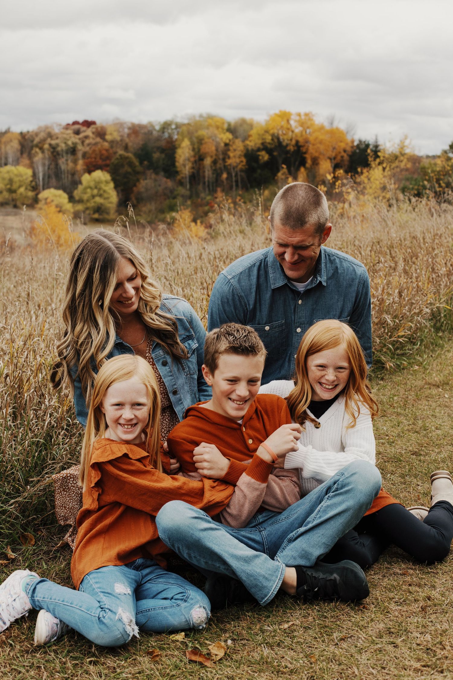Happy family of five laughing together while sitting in autumn field with fall colors.