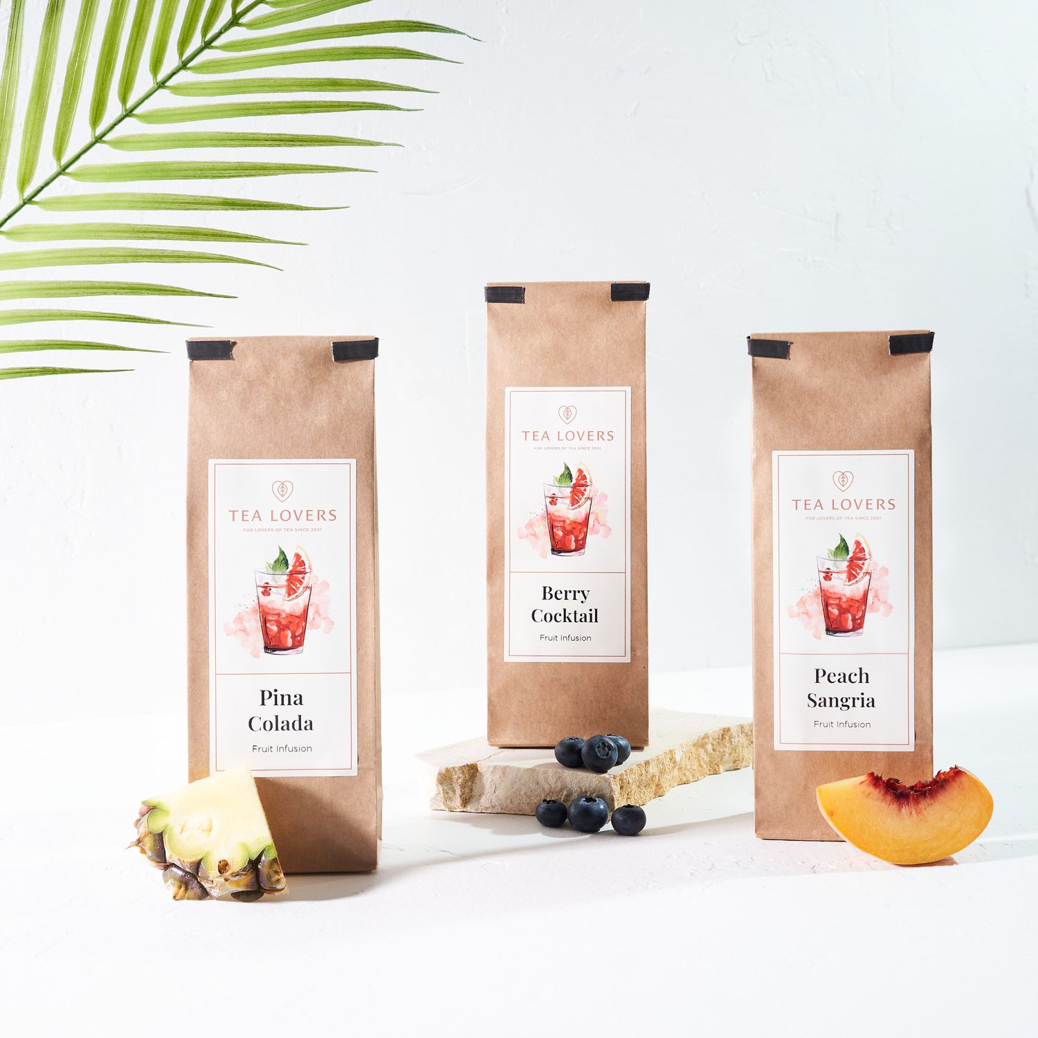 Three tea packages with fruit illustrations and text on brown paper bags.