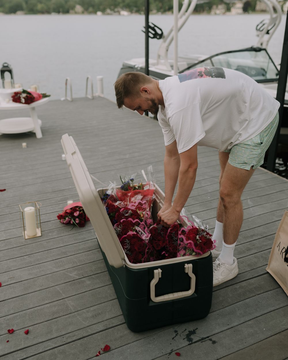 A decorative setup being prepared on a waterfront deck with lanterns and rose petals.