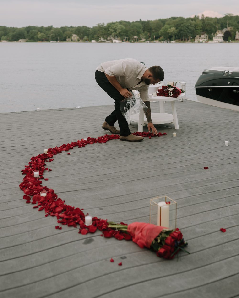 Rose petals arranged in a heart shape with candles on a waterfront deck at dusk.
