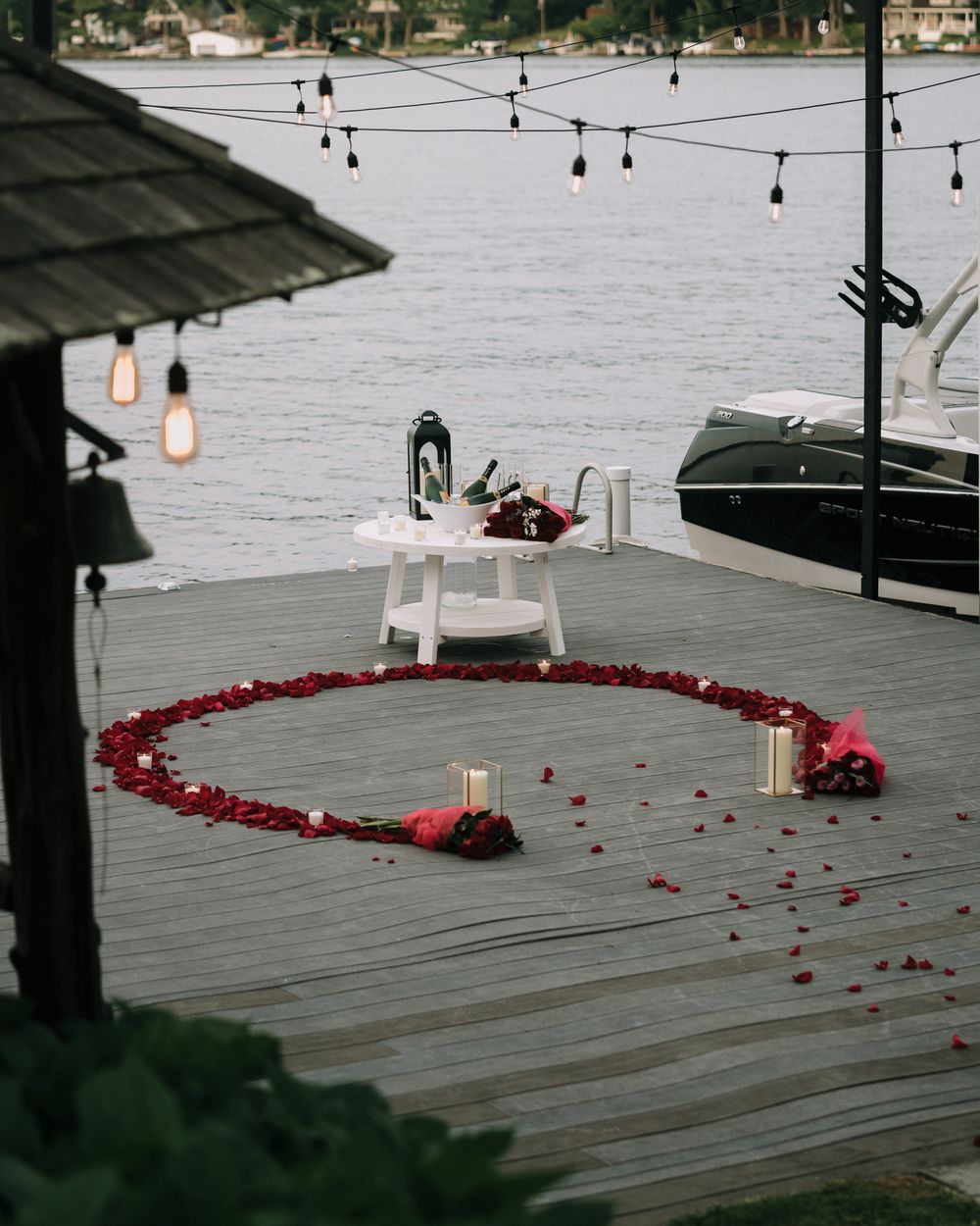 String lights illuminate a lakeside deck decorated with red rose petals and candles.